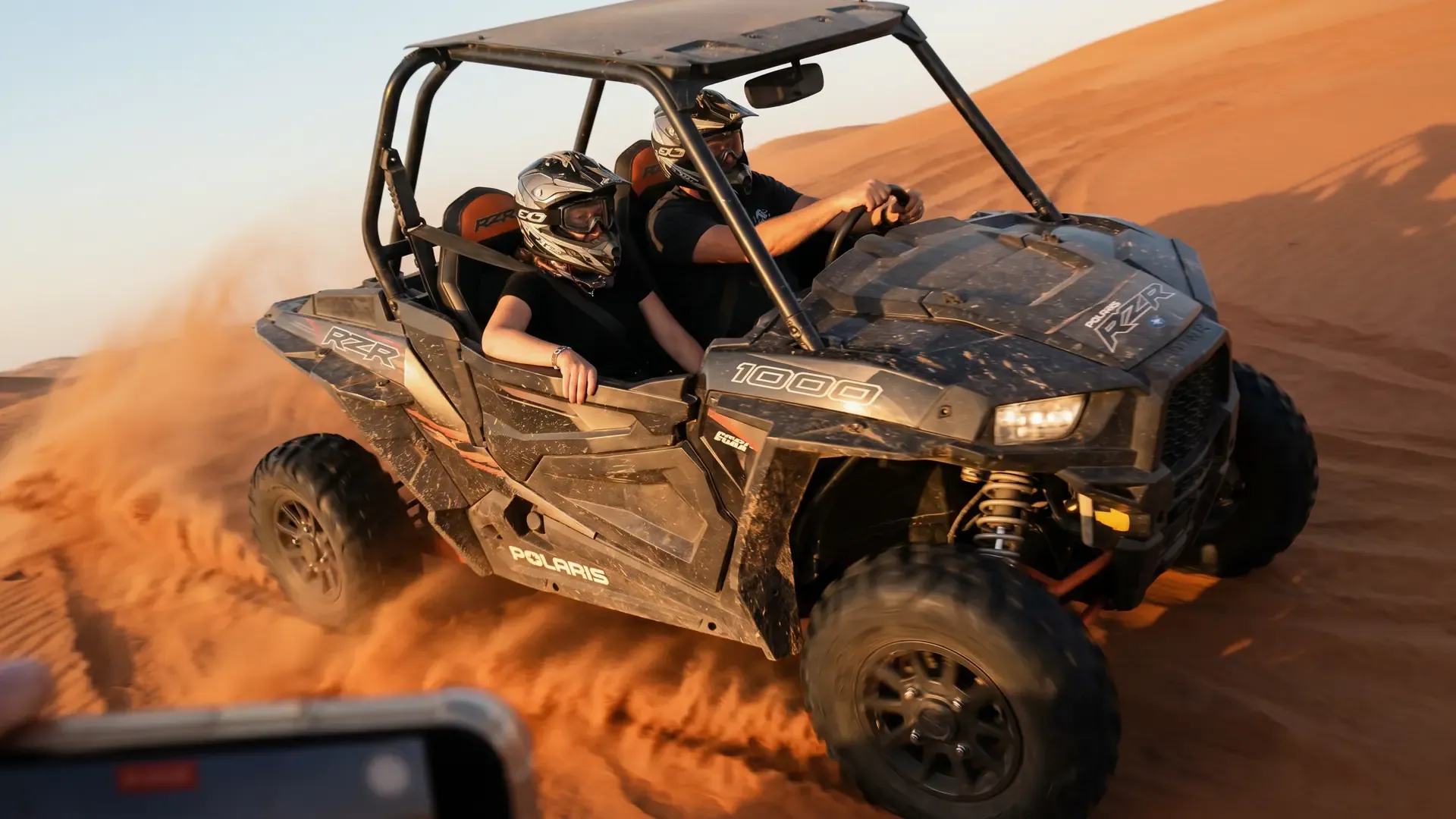 Driver and passenger in a Polaris RZR 1000 buggy with helmets and goggles on a desert dune