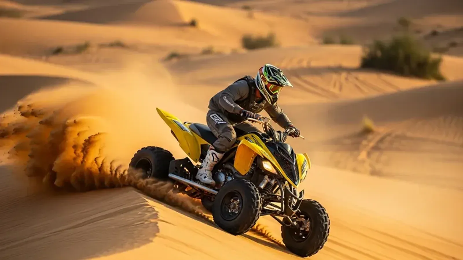 Rider in a helmet and goggles climbing a dune on a yellow quad bike