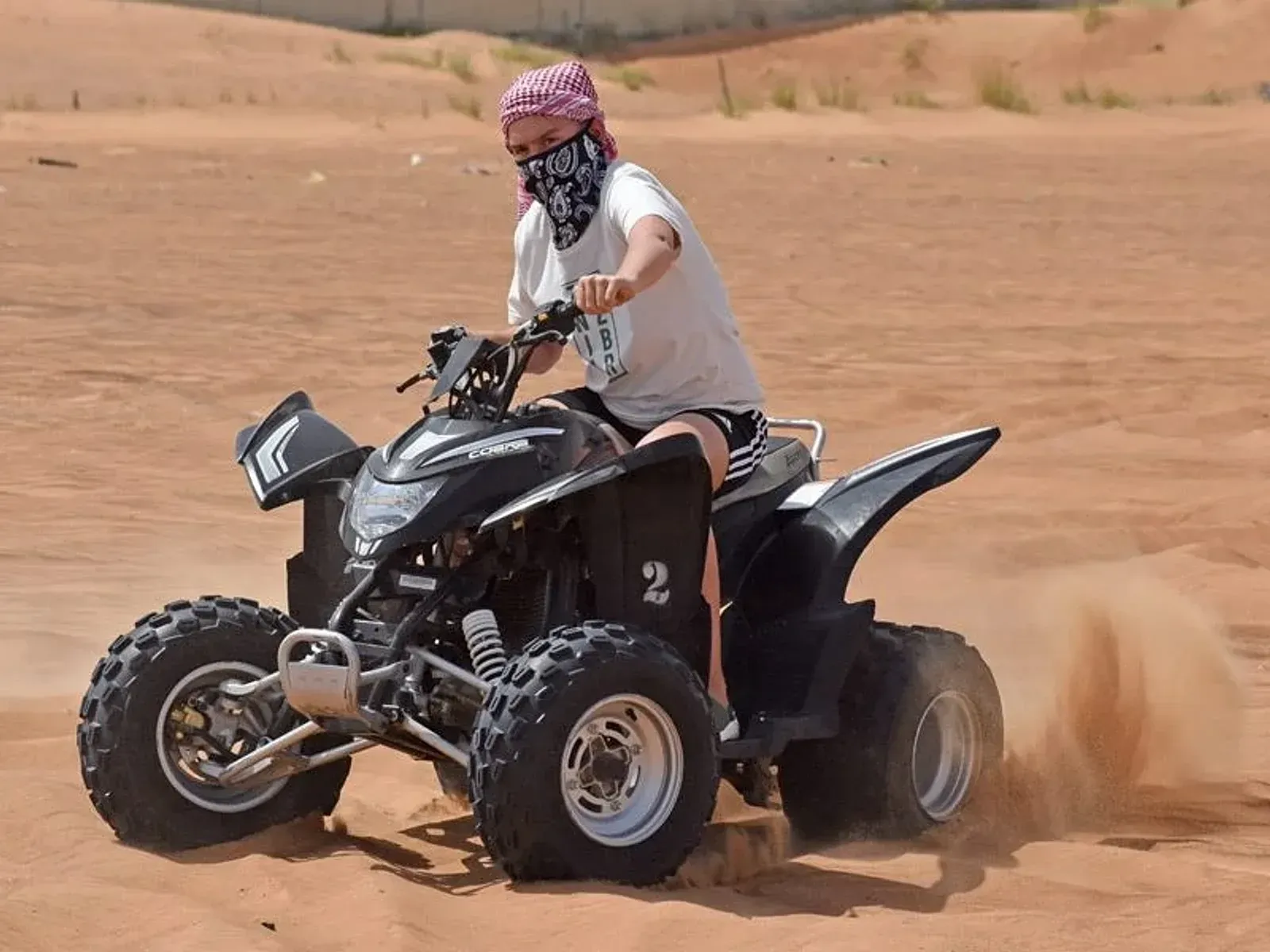 Rider on a black single-seater quad bike kicking up sand on a dune