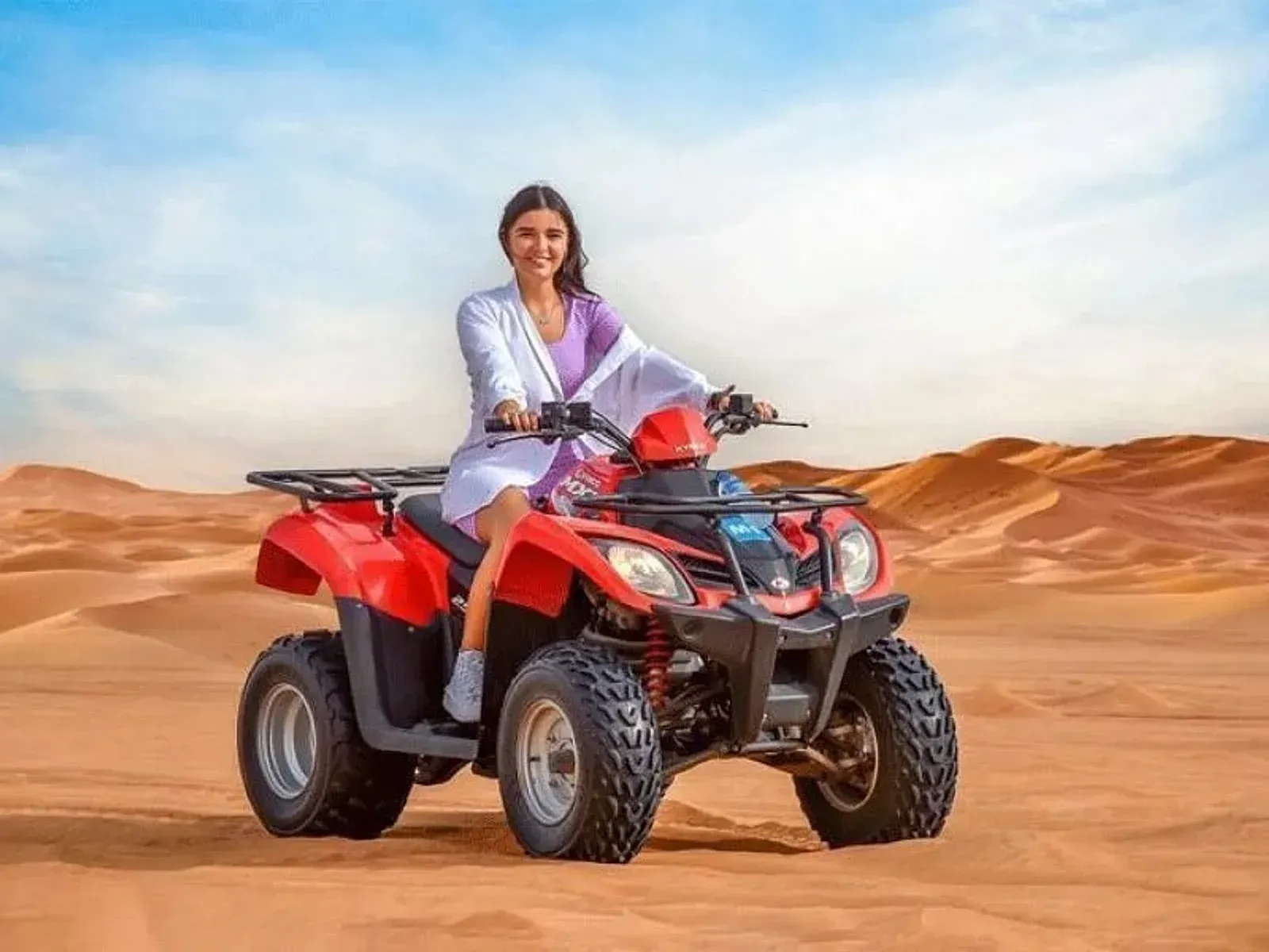 Smiling rider on a red single-seater quad bike parked on open desert sand with dunes behind